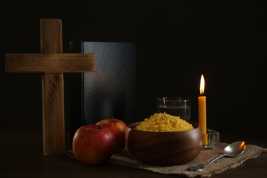 Millet, apple, water, burning candle, Bible and cross on wooden table. Great Lent season