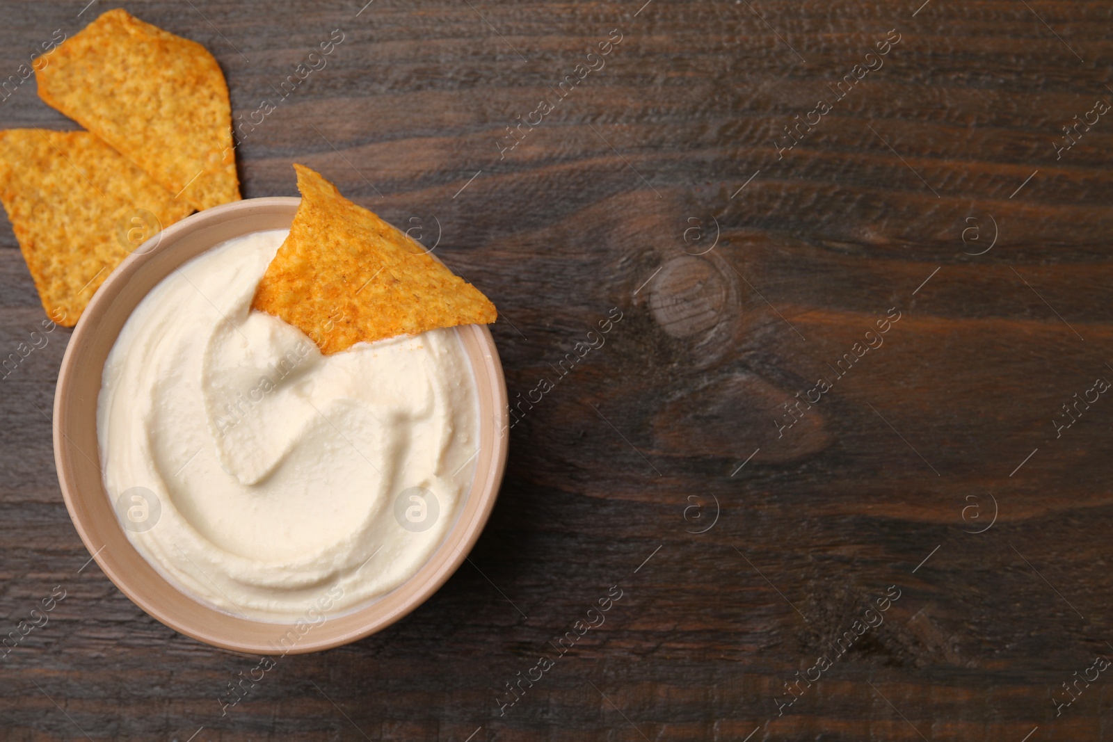 Photo of Delicious tofu sauce served with nachos chips in bowl on wooden table, top view. Space for text