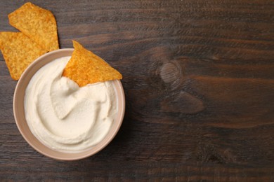 Photo of Delicious tofu sauce served with nachos chips in bowl on wooden table, top view. Space for text