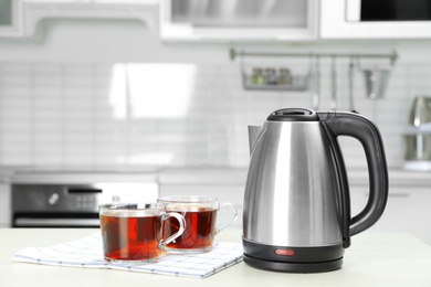 Photo of Modern electric kettle and cups of tea on white wooden table in kitchen. Space for text