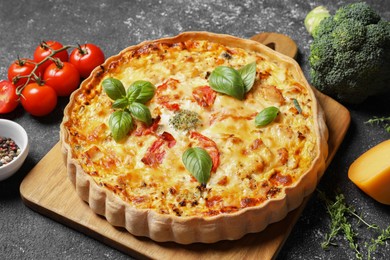 Photo of Tasty quiche with tomatoes, basil and cheese served on dark textured table, closeup
