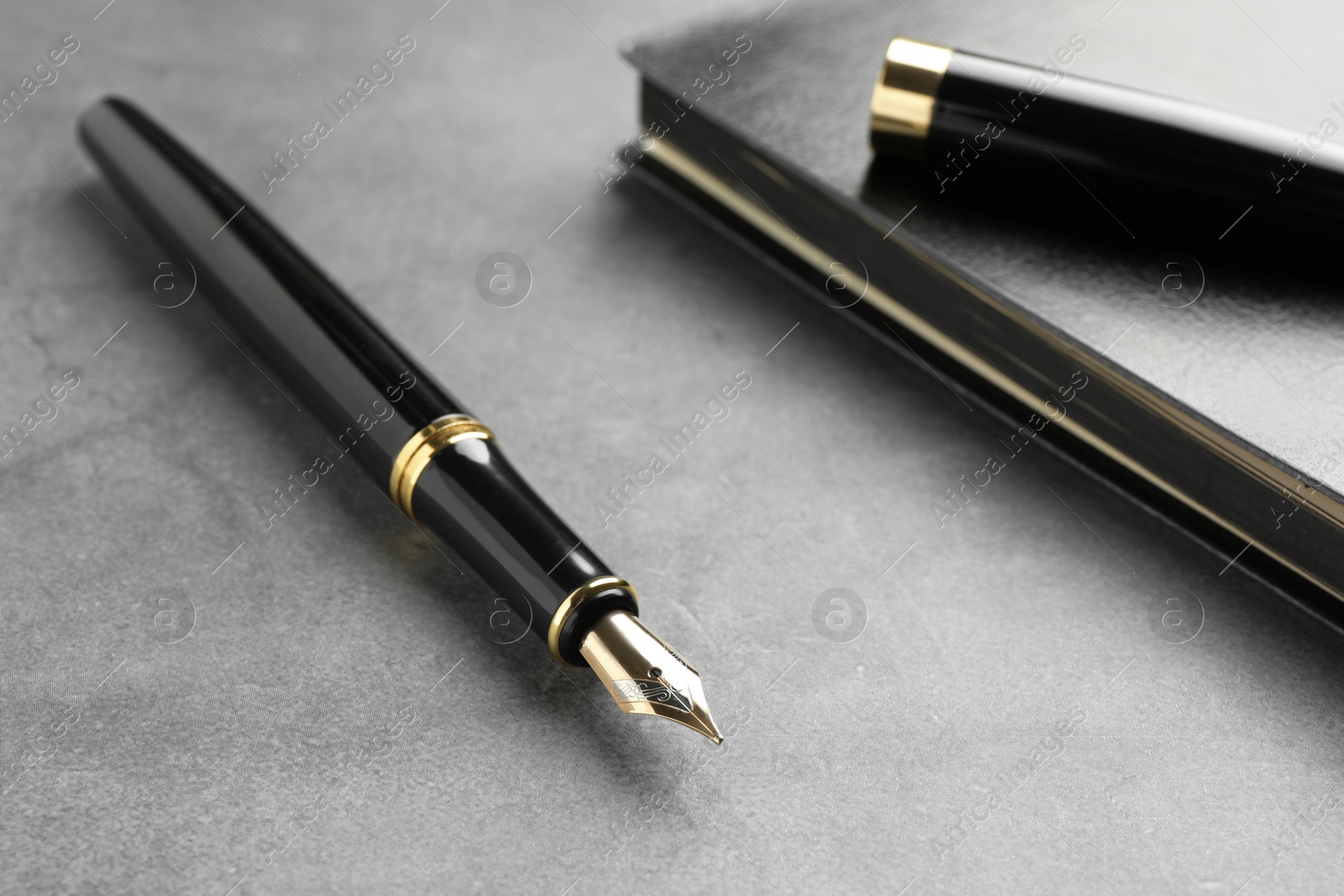 Photo of Stylish fountain pen and notebook on light grey textured table, closeup