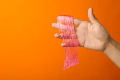 Photo of Woman playing with pink slime on orange background, closeup. Antistress toy
