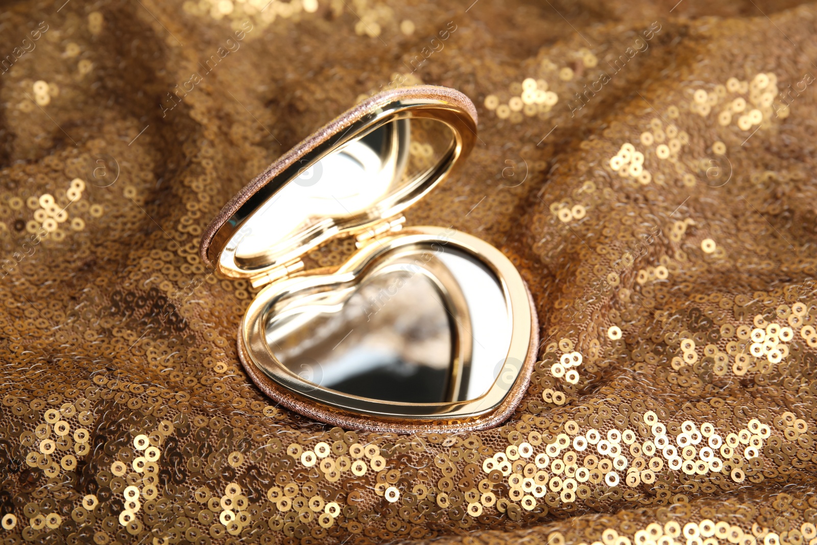 Photo of Stylish heart shaped cosmetic pocket mirror on gold fabric