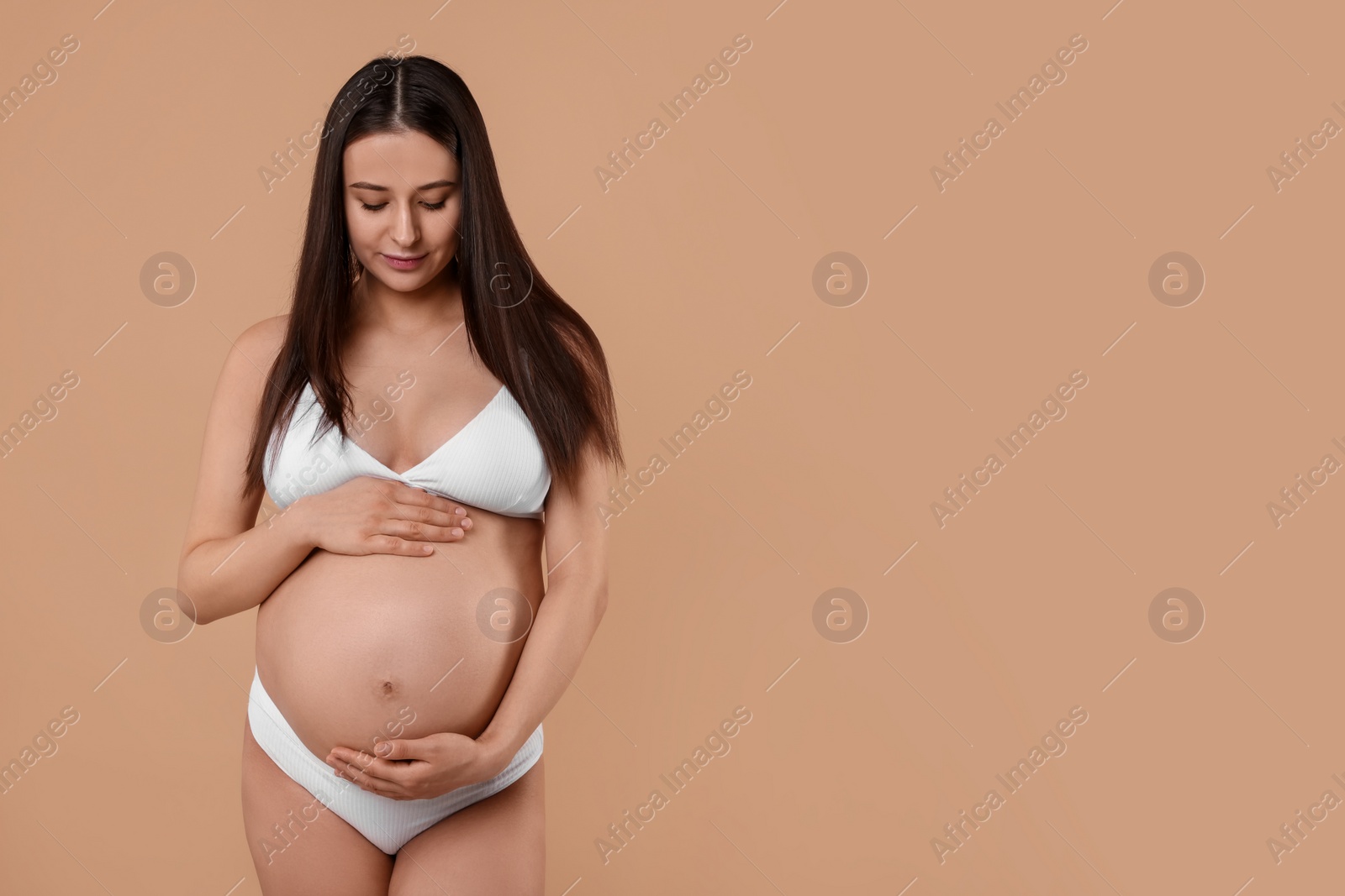 Photo of Beautiful pregnant woman in stylish comfortable underwear on beige background, space for text