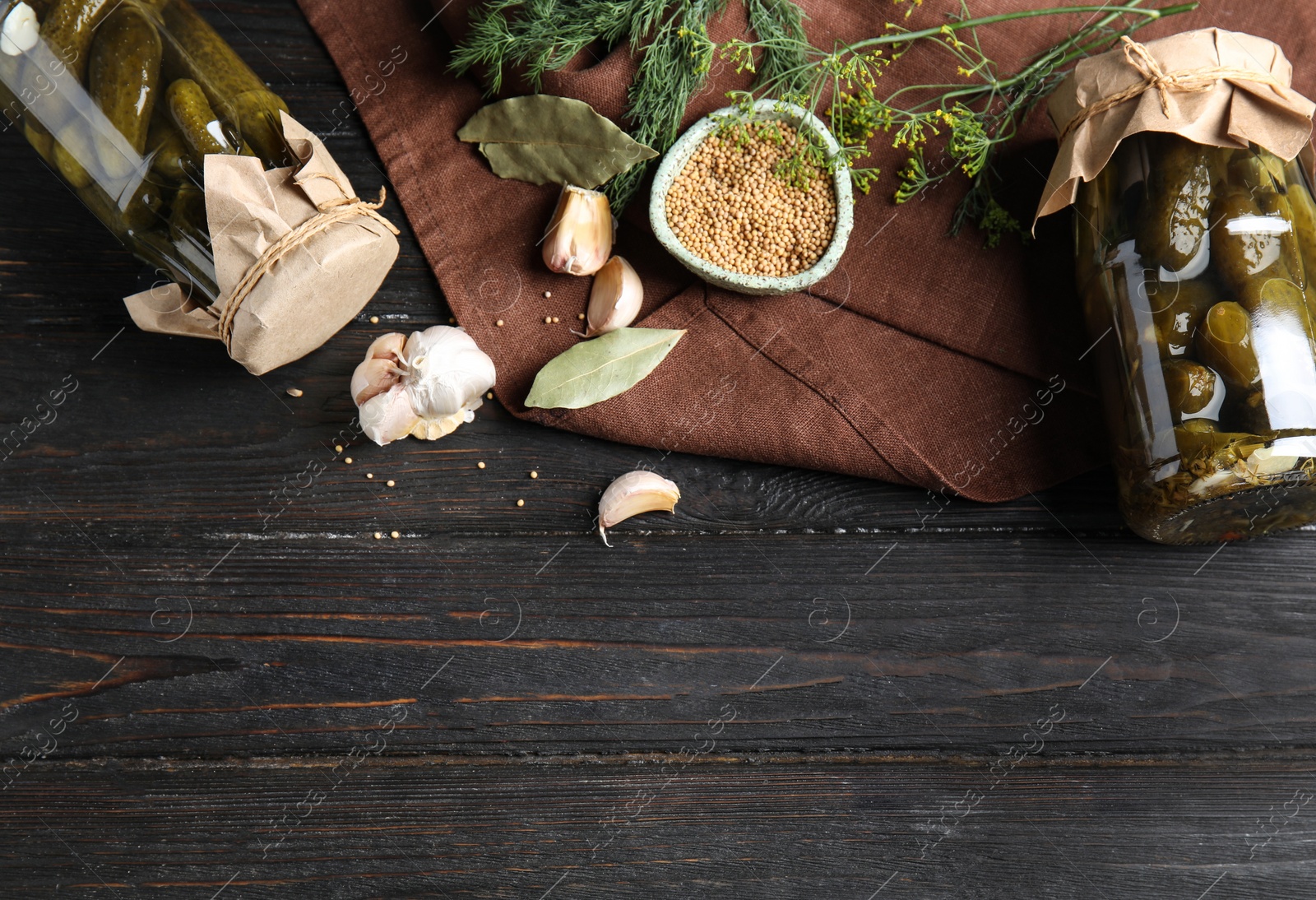 Photo of Flat lay composition with jars of pickled cucumbers on black wooden table, space for text