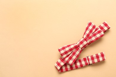 Stylish red and white gingham bow tie on beige background, top view. Space for text