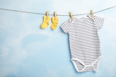 Baby clothes hanging on rope near color wall. Space for text