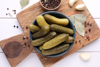 Photo of Tasty pickled cucumbers in bowl and ingredients on white wooden table, flat lay