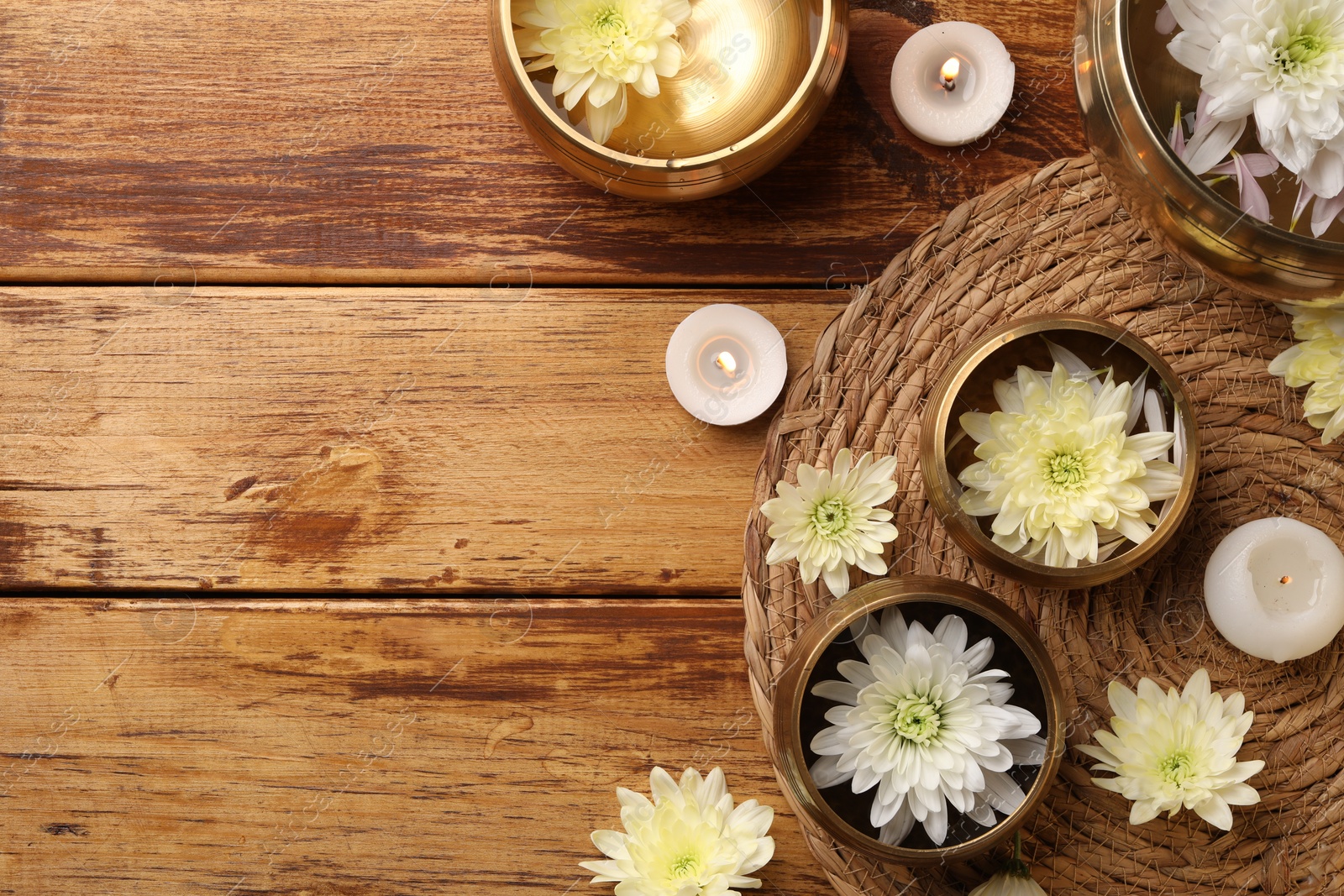 Photo of Tibetan singing bowls, beautiful chrysanthemum flowers and burning candles on wooden table, flat lay. Space for text
