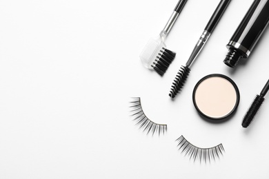 Composition with false eyelashes and other makeup products on white background, top view
