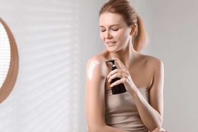 Photo of Beautiful woman applying body cream onto shoulder indoors, space for text