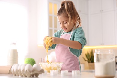 Photo of Little girl making dough at table in kitchen