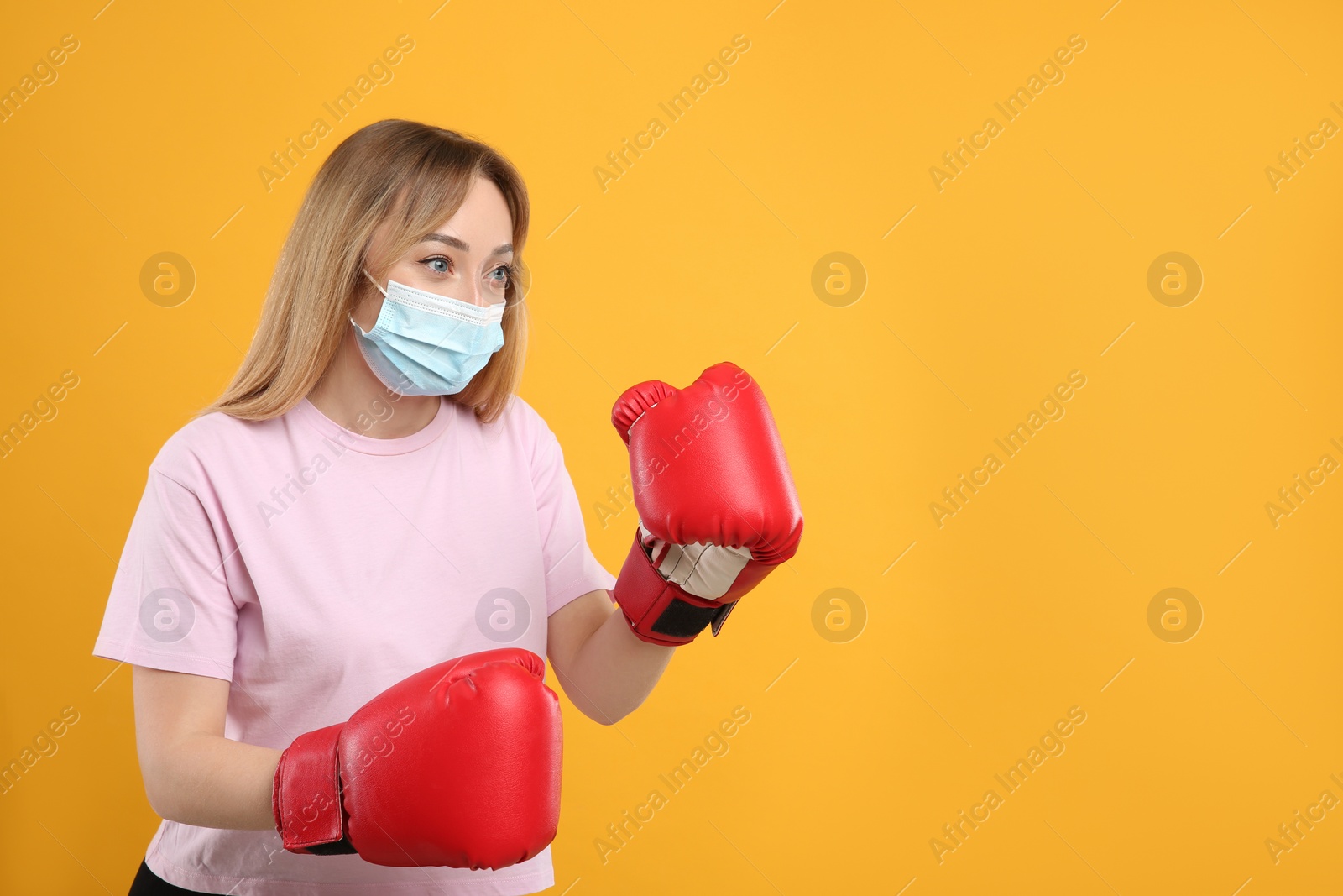 Photo of Woman with protective mask and boxing gloves on yellow background, space for text. Strong immunity concept