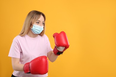 Photo of Woman with protective mask and boxing gloves on yellow background, space for text. Strong immunity concept