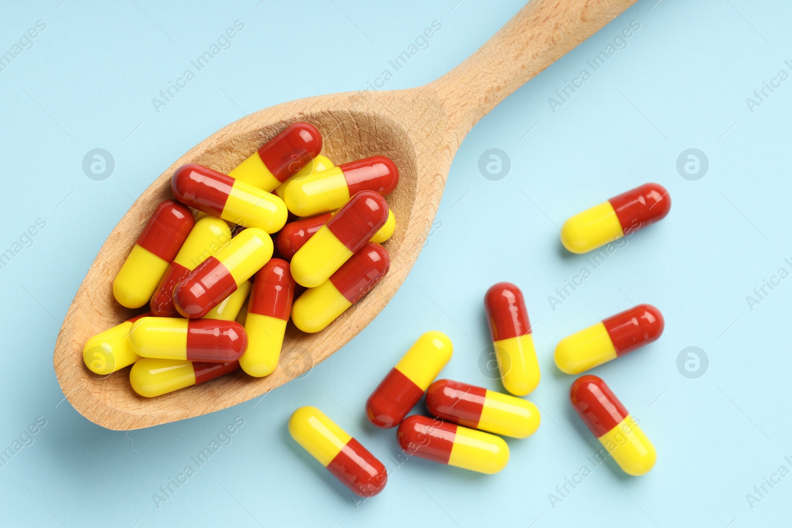 Photo of Antibiotic pills and spoon on light blue background, top view