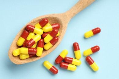 Antibiotic pills and spoon on light blue background, top view