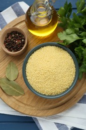 Photo of Bowl of raw couscous and ingredients on blue wooden table, flat lay