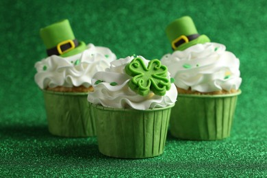 St. Patrick's day party. Tasty festively decorated cupcakes on shiny green surface, closeup