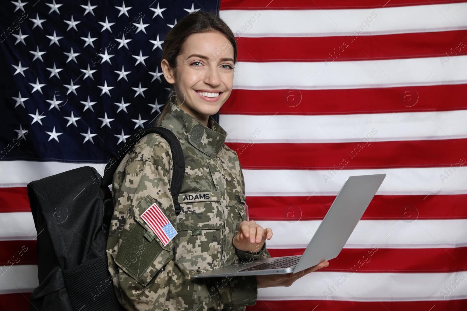 Photo of Female cadet with backpack and laptop against American flag. Military education