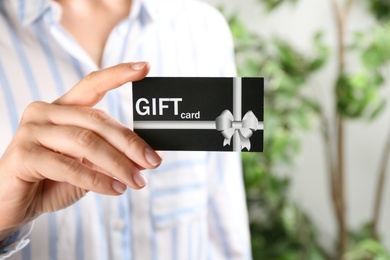 Woman with gift card on blurred background, closeup