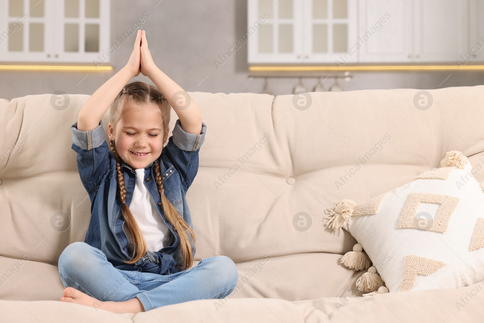 Photo of Little girl meditating on soft sofa at home, space for text