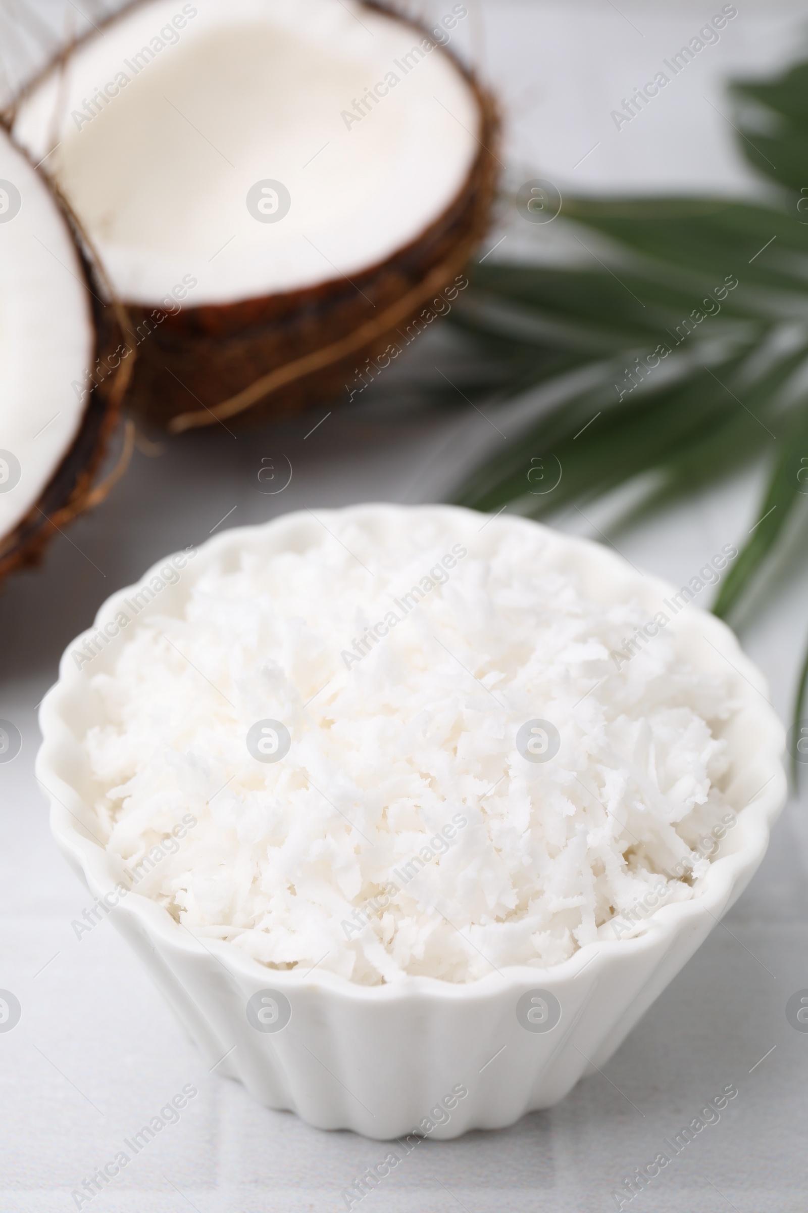 Photo of Coconut flakes in bowl, nuts and palm leaf on white table, closeup