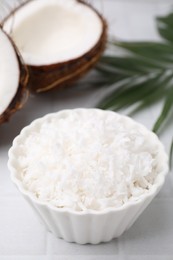 Photo of Coconut flakes in bowl, nuts and palm leaf on white table, closeup