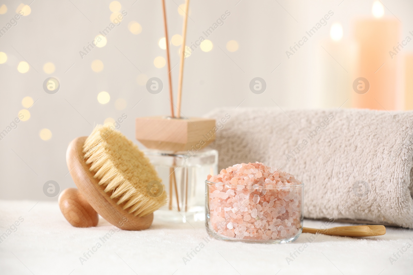 Photo of Spa composition. Sea salt, brush, towel and reed air freshener on soft white surface