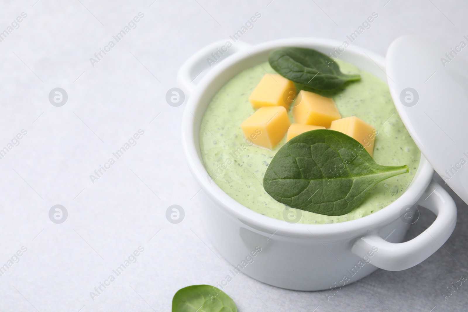 Photo of Delicious spinach cream soup with cheese in bowl on light grey table, closeup. Space for text