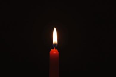 Photo of Wax candle burning on black background, closeup