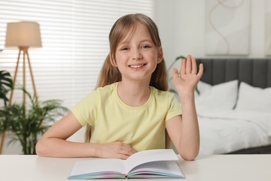 Happy little girl waving hello during online lesson indoors, view from web camera