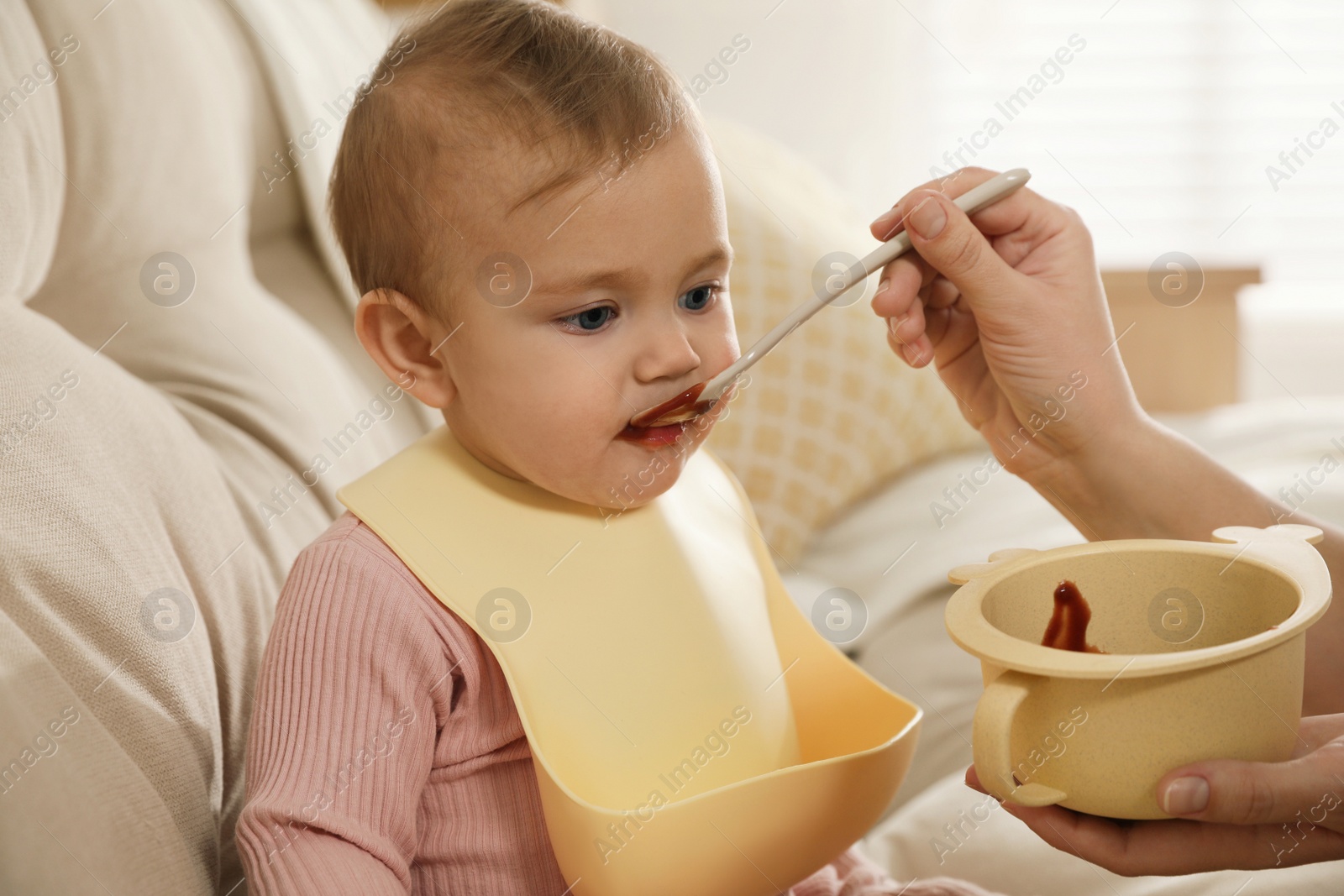 Photo of Mother feeding her little baby at home. Kid wearing silicone bib