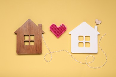 Photo of Decorative hearts and cord between two house models on pale yellow background symbolizing connection in long-distance relationship
