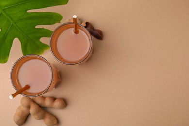 Photo of Tamarind juice, fresh fruits and green leaf on pale brown background, flat lay. Space for text