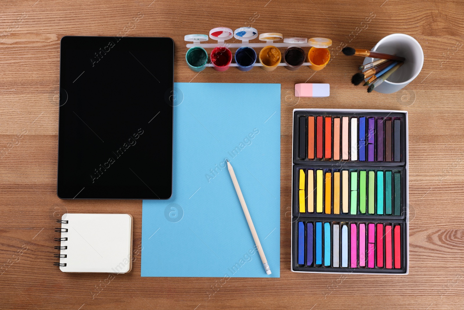 Photo of Blank sheet of paper, colorful chalk pastels, tablet and other drawing tools on wooden table, flat lay. Modern artist's workplace