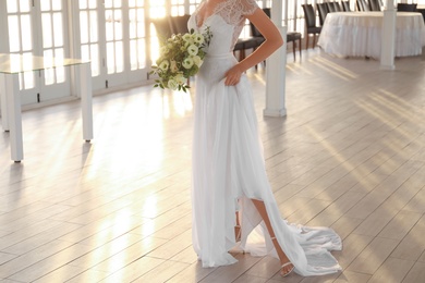 Photo of Bride in beautiful wedding dress with bouquet in restaurant, closeup