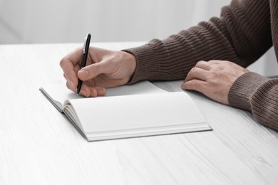 Photo of Man writing in notebook at white wooden table, closeup