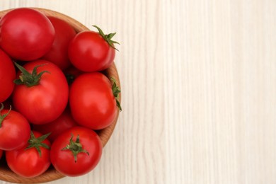 Photo of Bowl of ripe red tomatoes on light wooden table, top view. Space for text