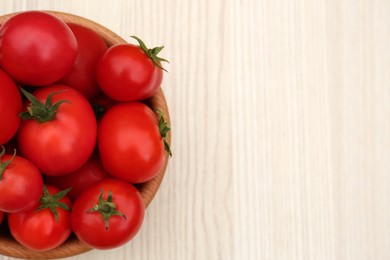 Bowl of ripe red tomatoes on light wooden table, top view. Space for text