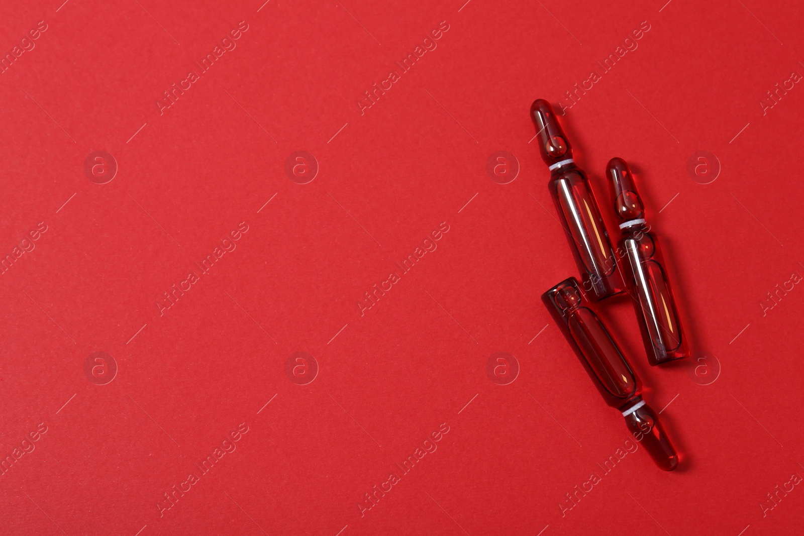 Photo of Glass ampoules with liquid on red background, top view. Space for text