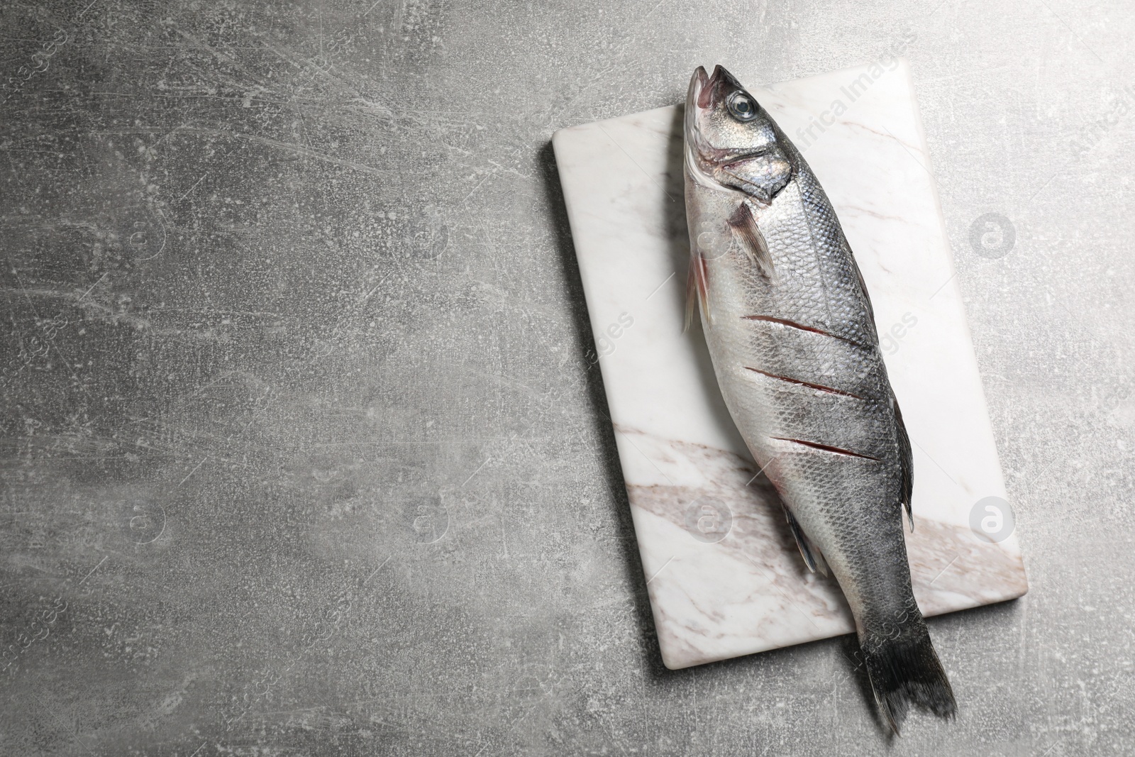 Photo of Fresh raw sea bass fish on light gray table, top view. Space for text