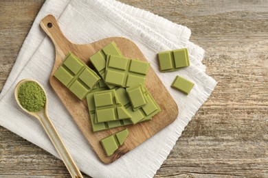 Photo of Pieces of tasty matcha chocolate bar and powder in spoon on wooden table, top view