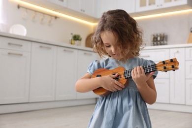 Photo of Little girl playing toy guitar in kitchen. Space for text