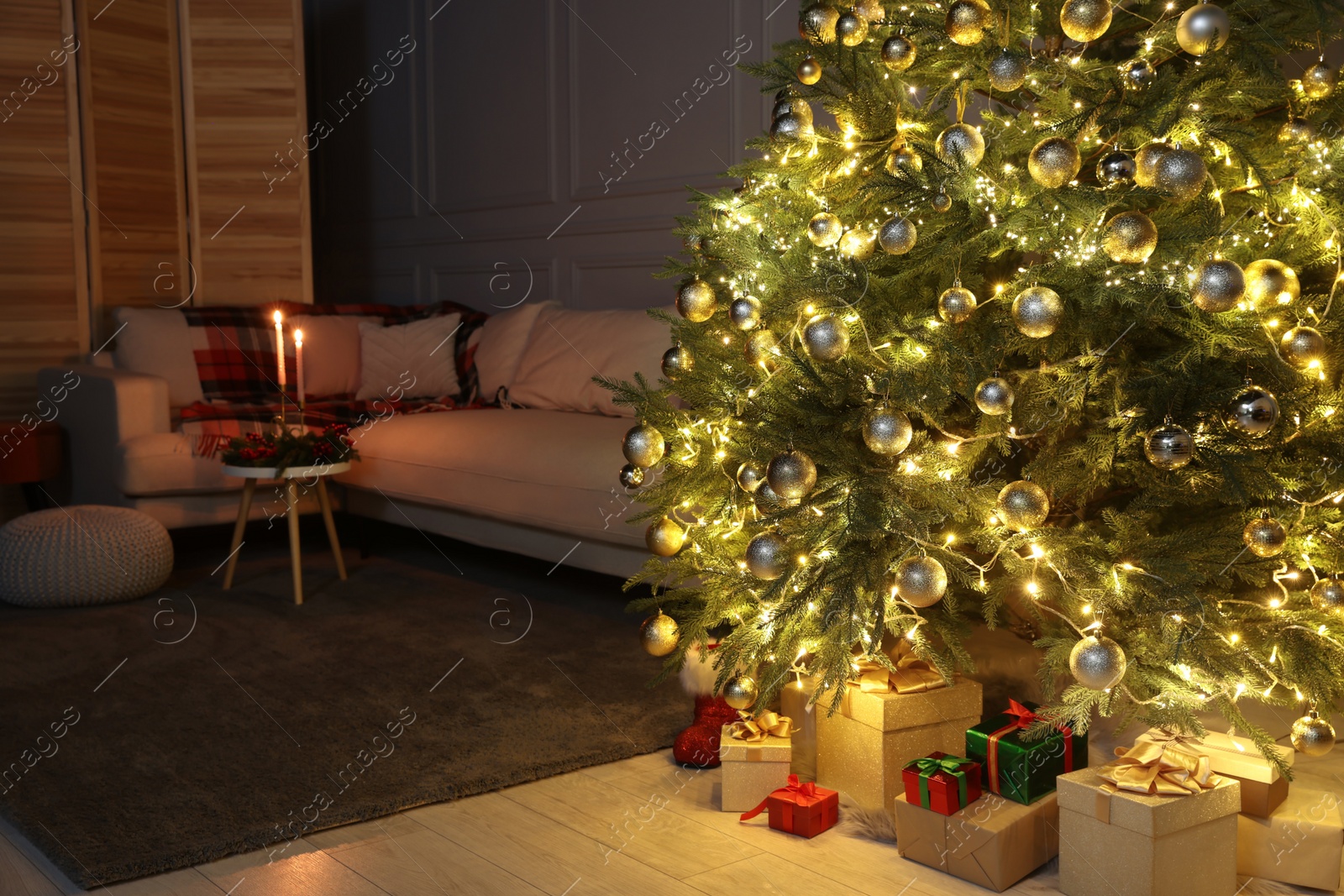 Photo of Beautiful glowing Christmas tree, gift boxes and sofa in living room