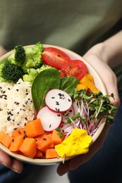 Photo of Woman holding bowl with different vegetables and rice, closeup. Vegan diet