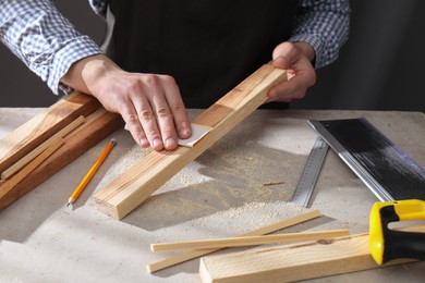 Photo of Man polishing wooden plank with sandpaper at grey table indoors, closeup