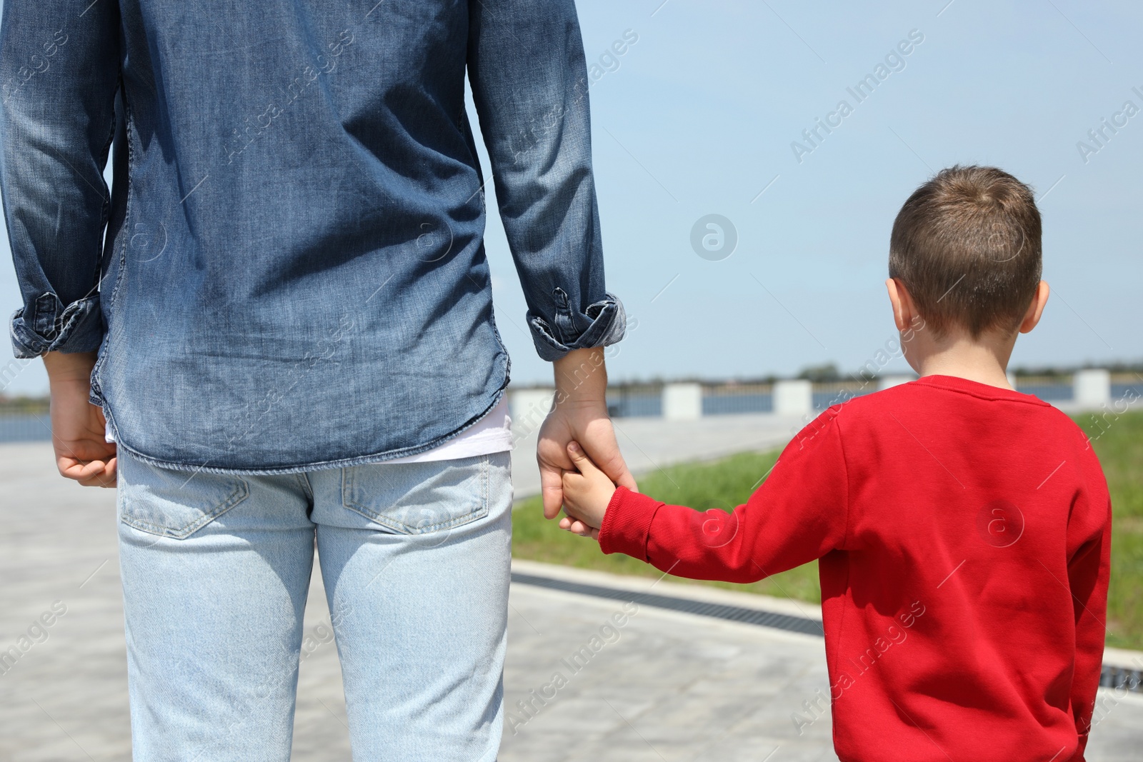 Photo of Little child holding hands with his father outdoors. Family weekend