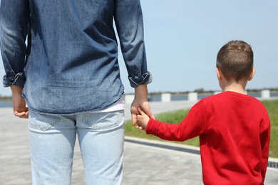 Photo of Little child holding hands with his father outdoors. Family weekend