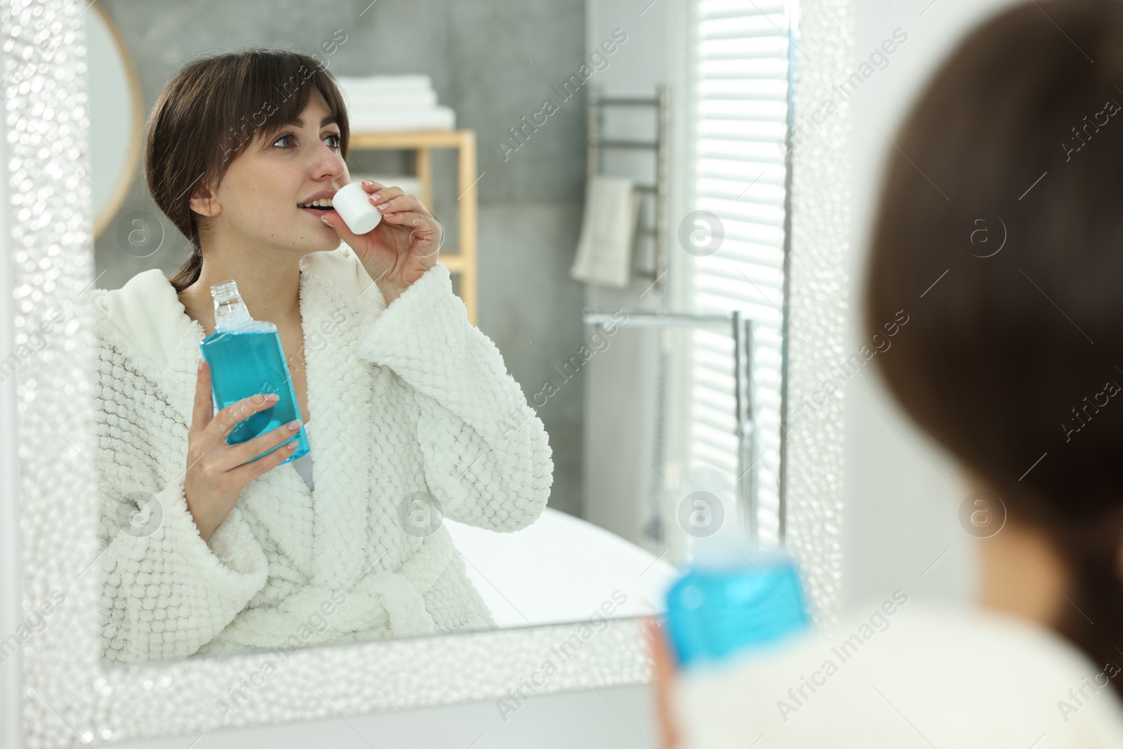 Photo of Young woman using mouthwash near mirror in bathroom